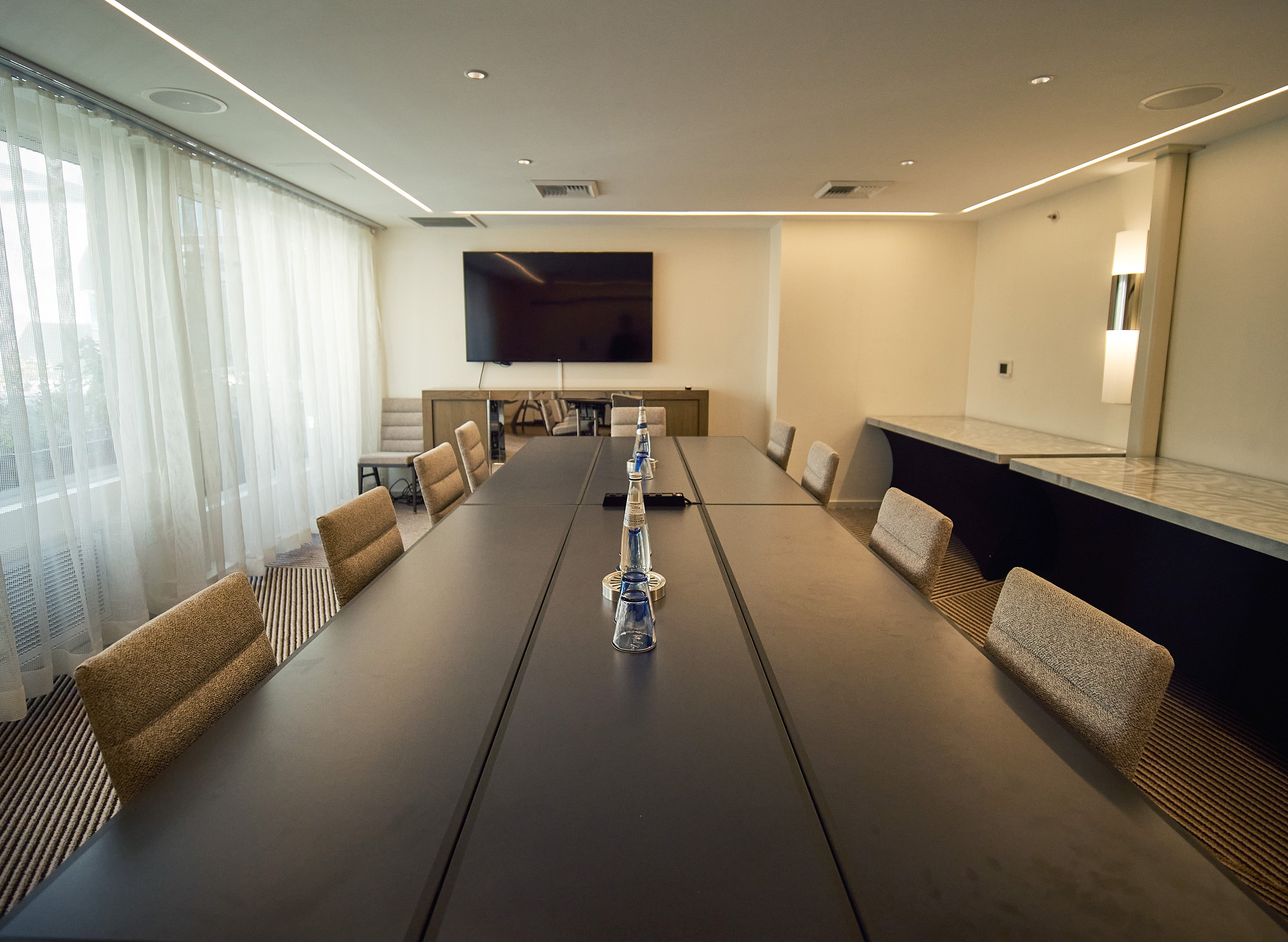 Spacious conference room featuring long table, neutral decor, and screen.