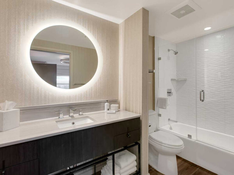 Bathroom with illuminated round mirror and shower.