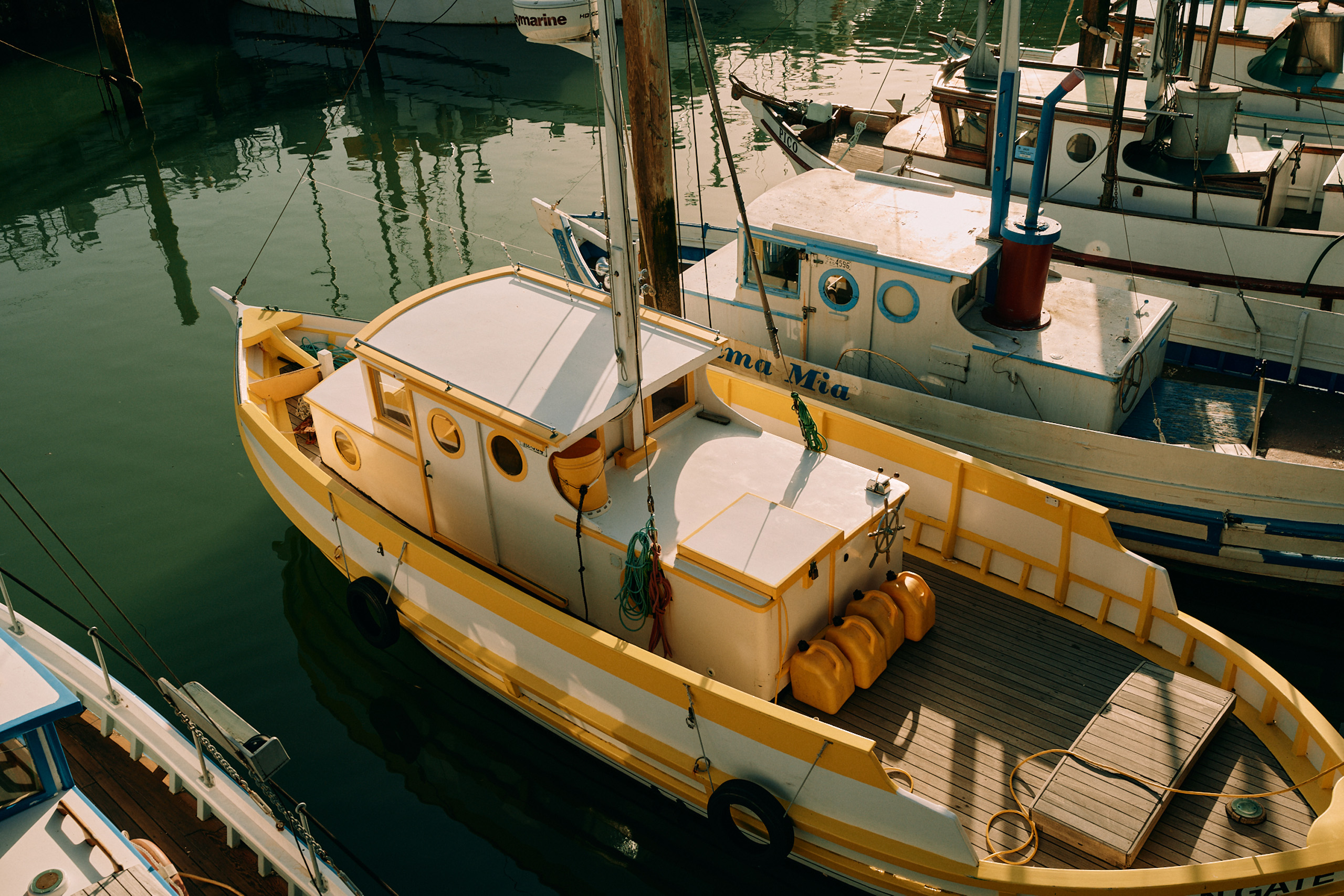 Yellow fishing boat docked beside other marina vessels.