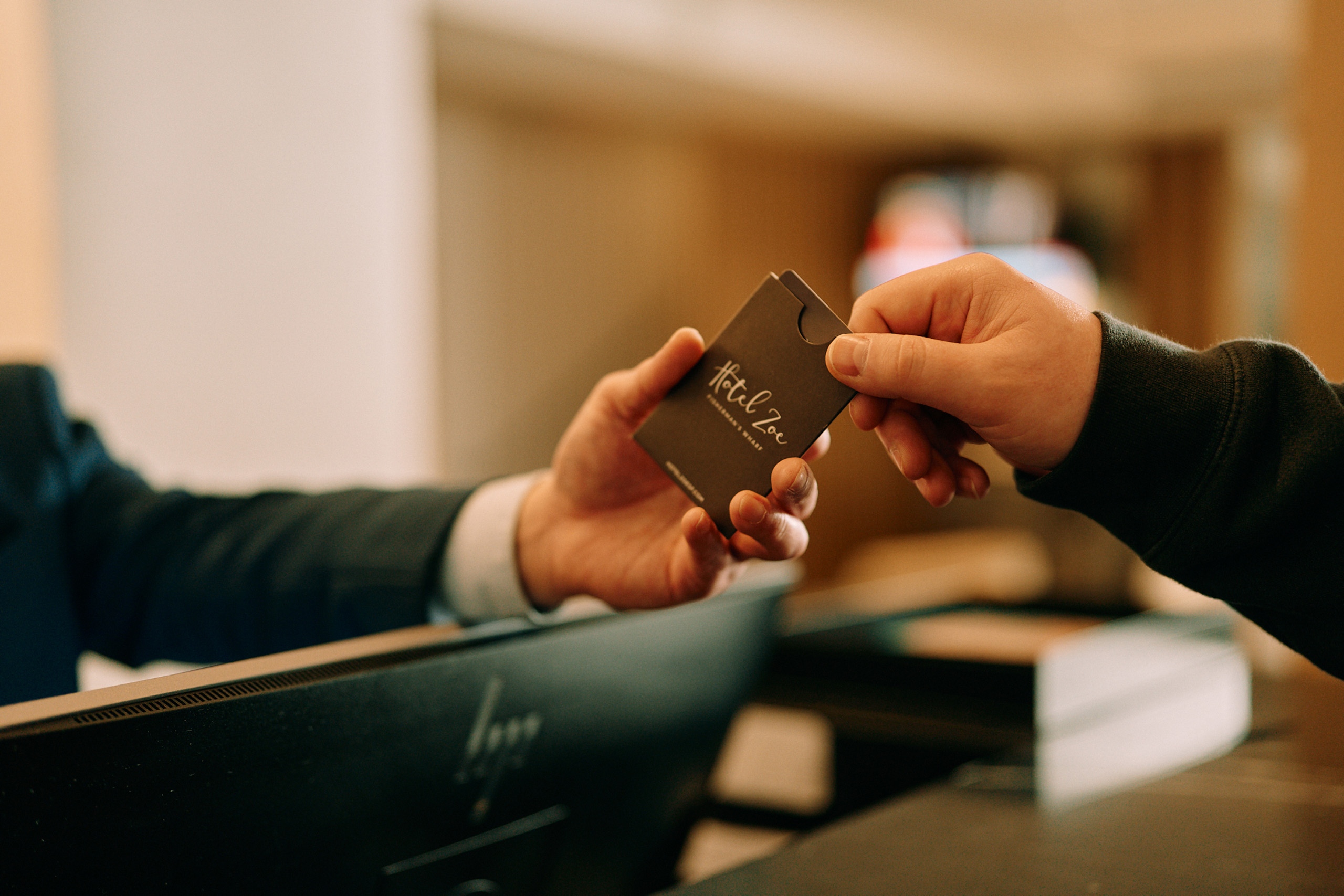 Hands exchanging a Hotel Zoe room key card.