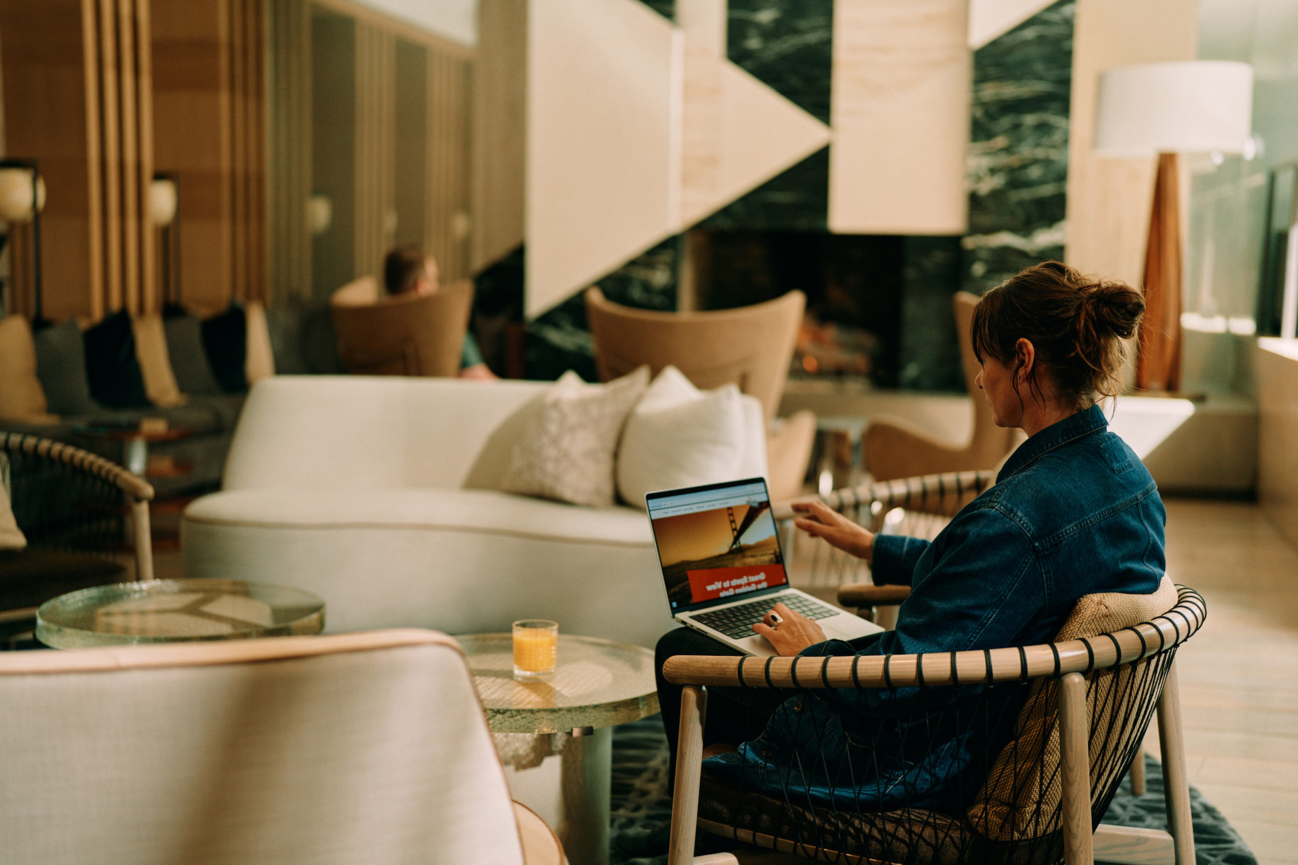 Woman working on laptop in hotel lounge area.