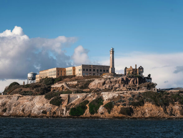 Rocky island with historic prison buildings under bright blue sky.