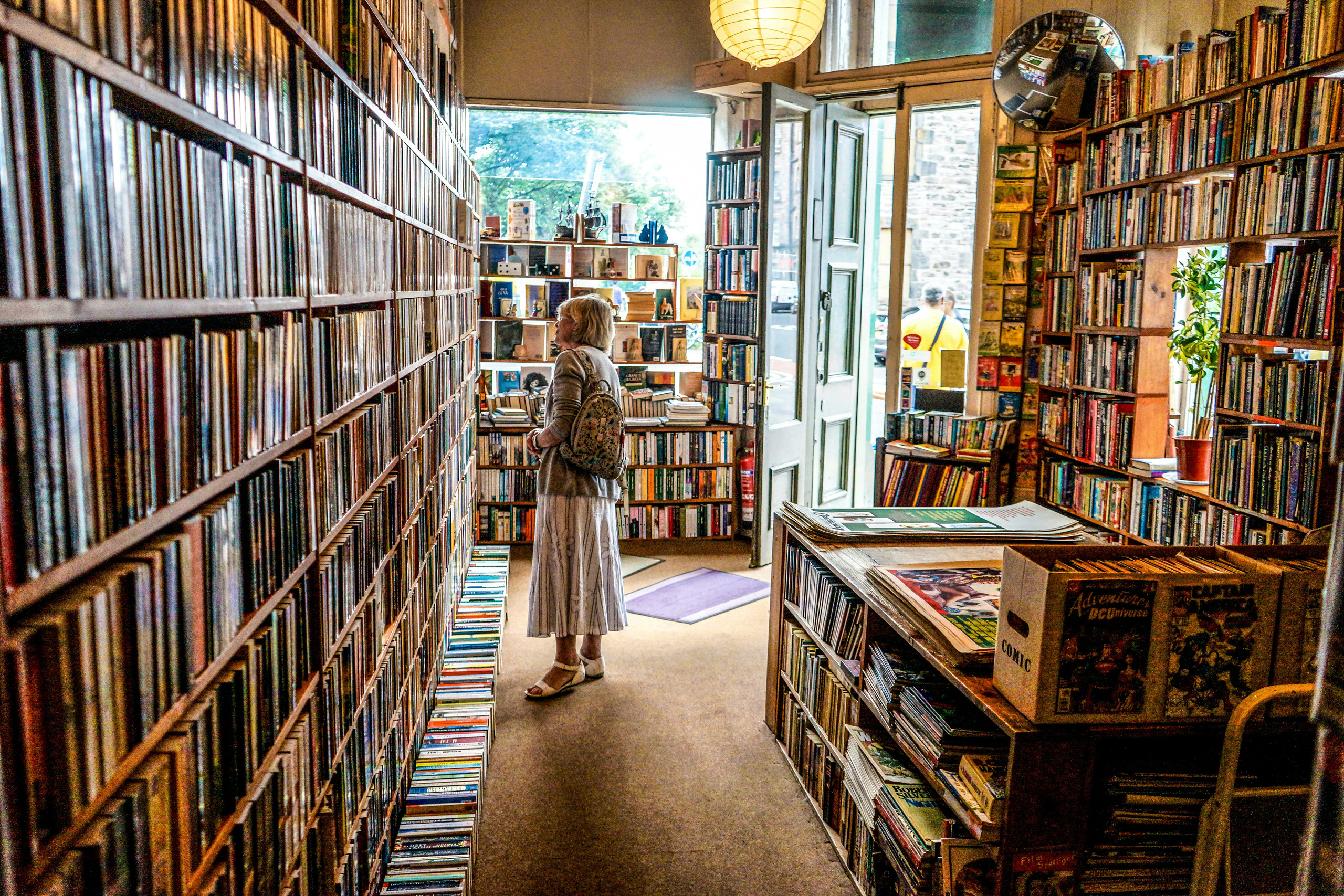 Woman browsing tall, colorful bookshelves in cozy independent bookstore.