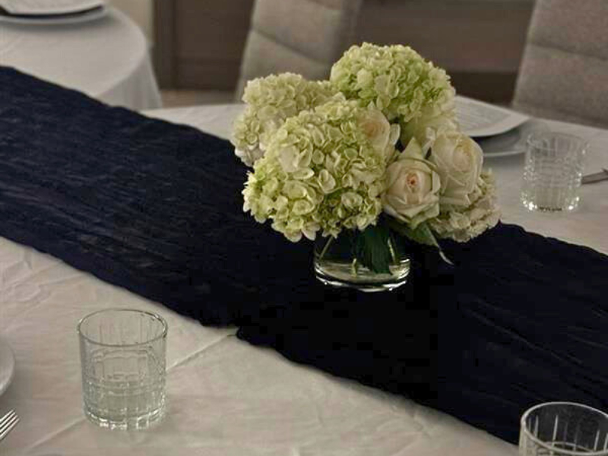 White floral centerpiece on dark table runner at event.