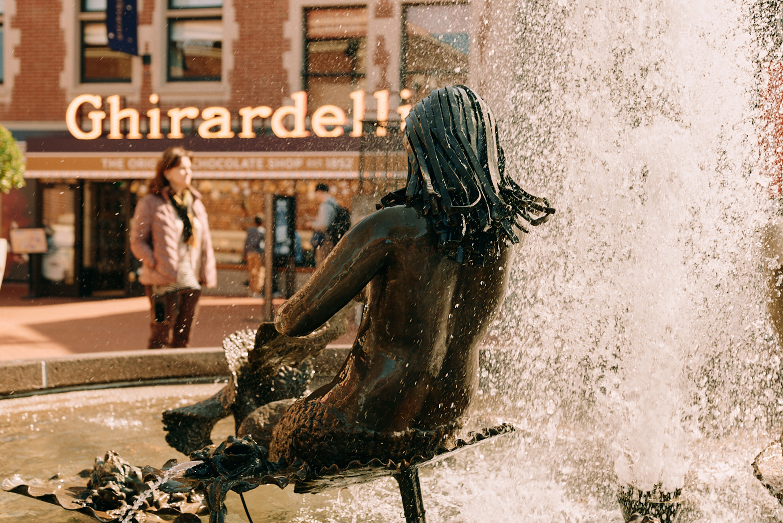 Bronze fountain statue splashed by water near Ghirardelli Square.
