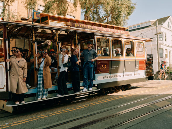 Tourists smiling and waving while riding San Francisco cable car.