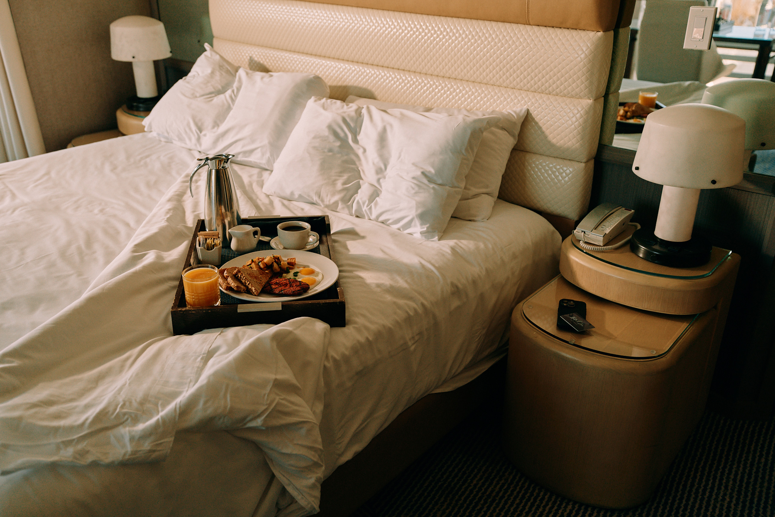 Breakfast tray with coffee and juice on a hotel bed.