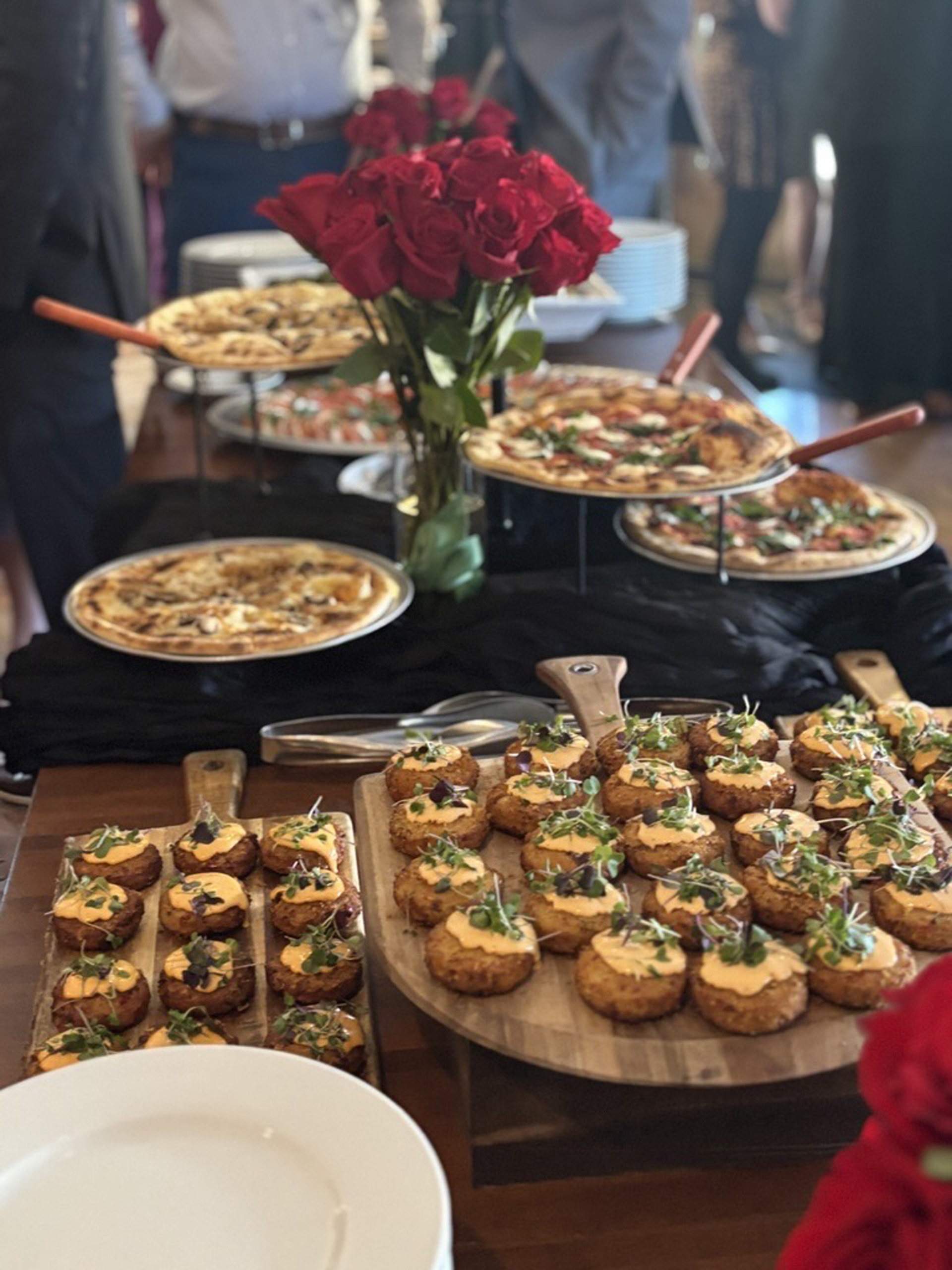 Buffet table with pizzas, appetizers, and red roses.