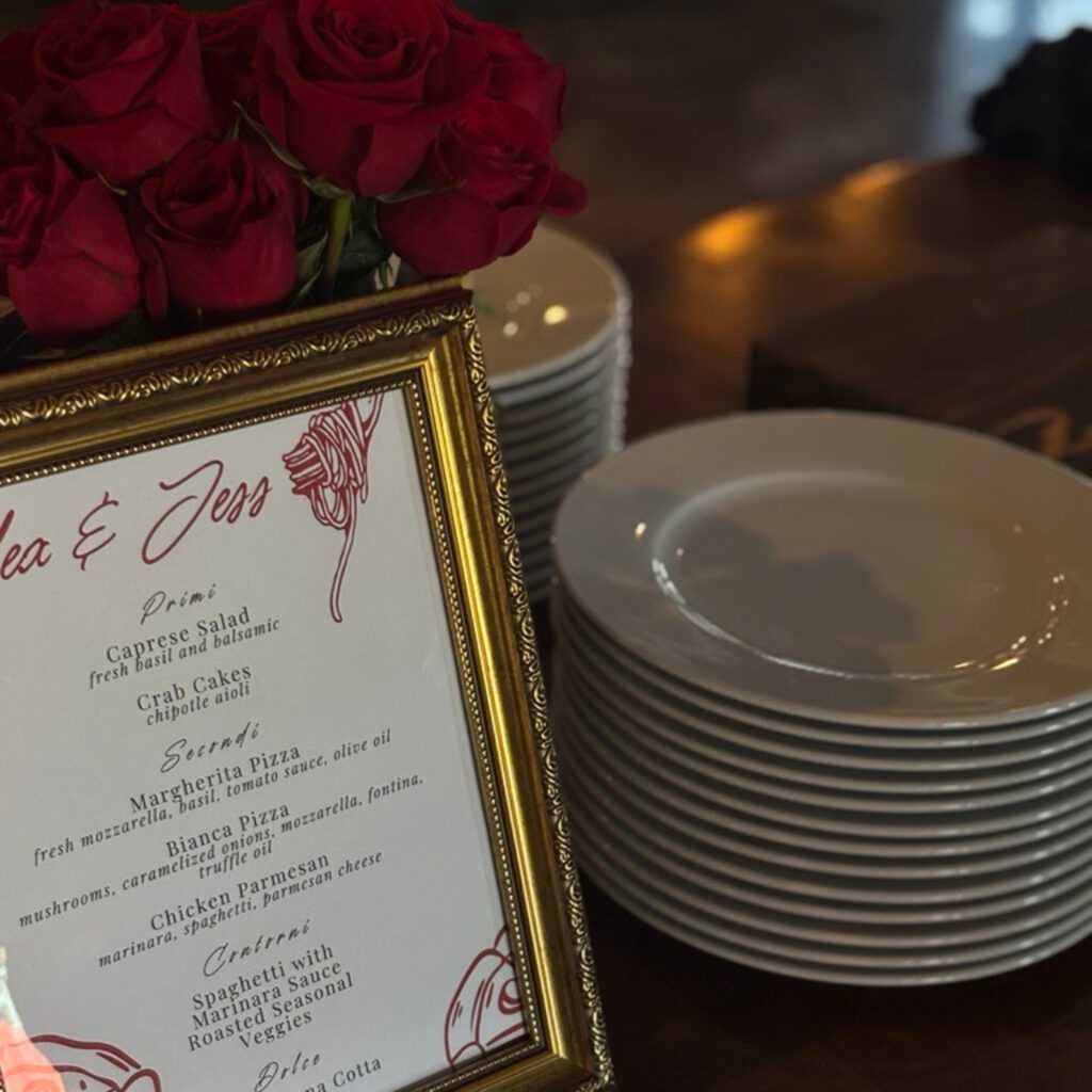 Framed event menu with red roses beside stacked plates.