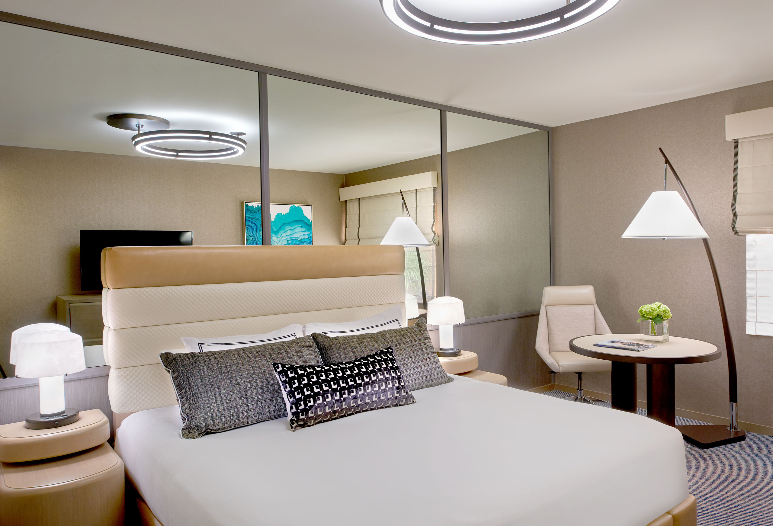 Modern hotel room with bed, seating area, and lighting.