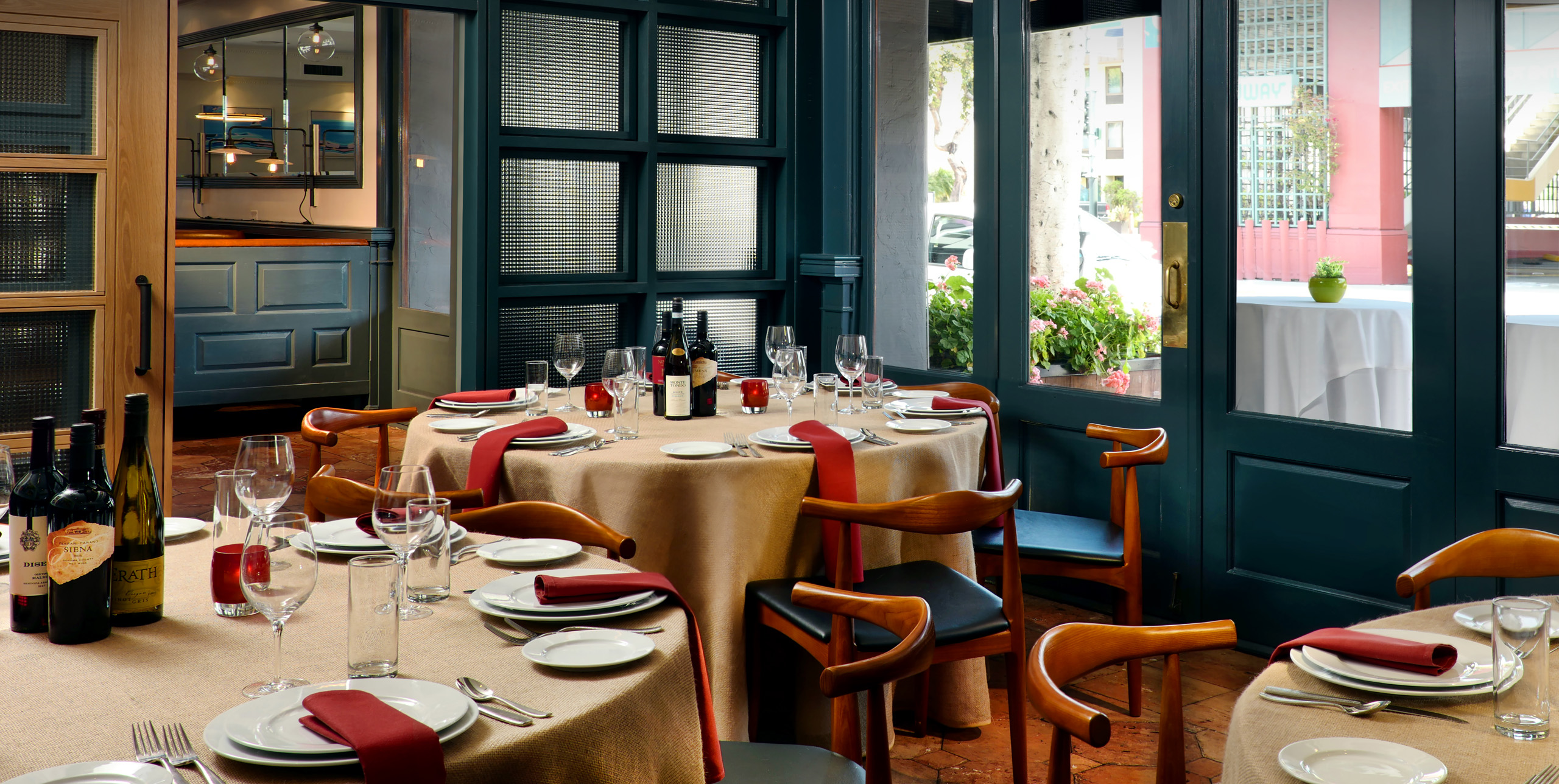 Round dining tables set with wine bottles, glasses, and red napkins.