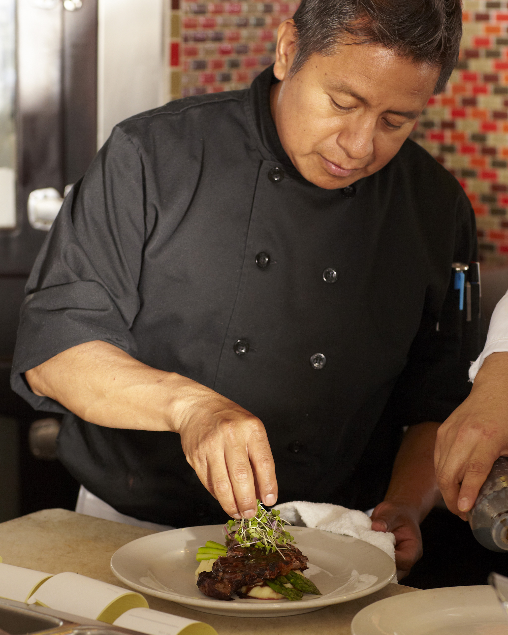 Chef carefully garnishing a plated dish in the kitchen.