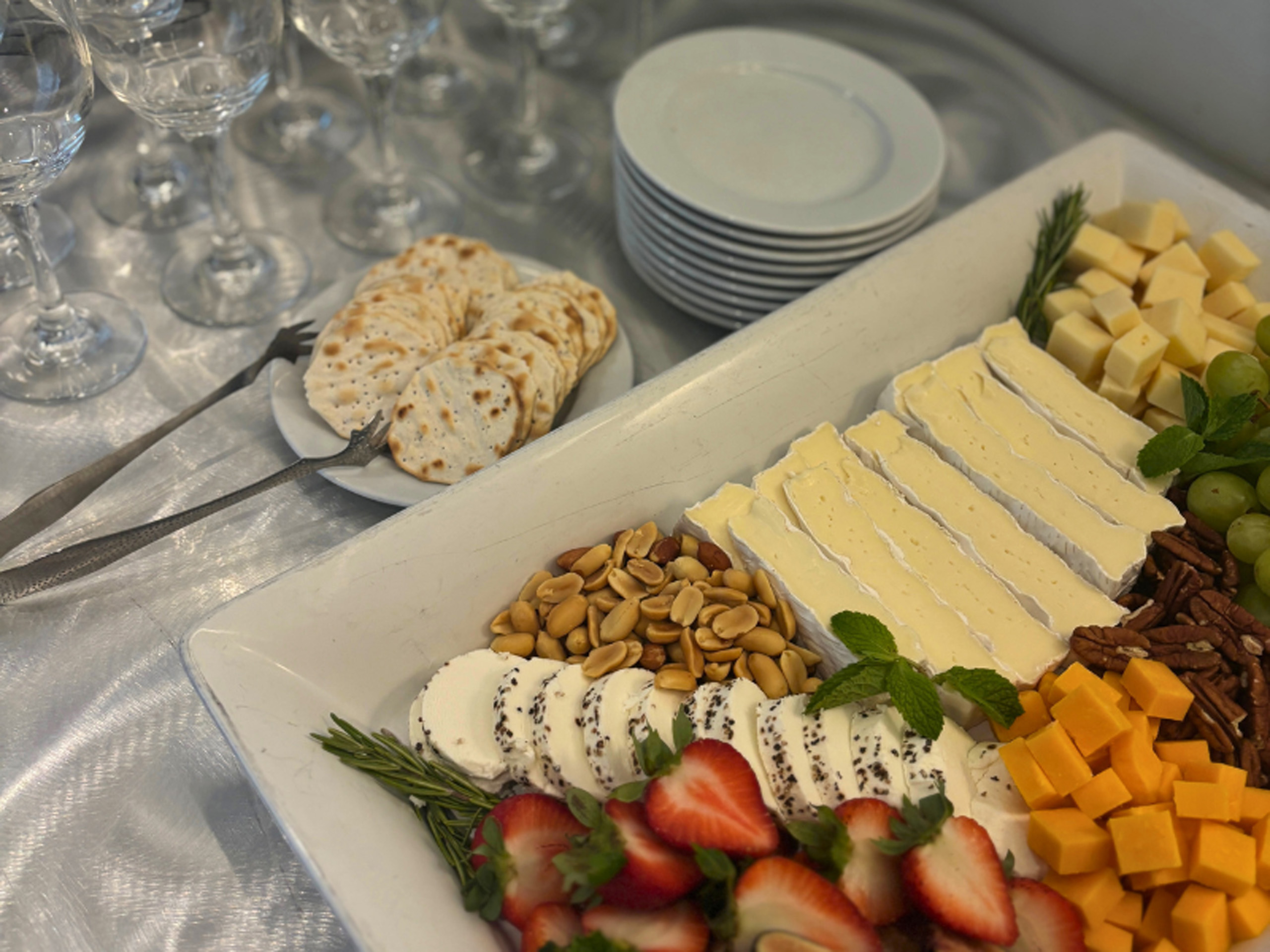 Cheese and fruit platter with crackers and glassware displayed.